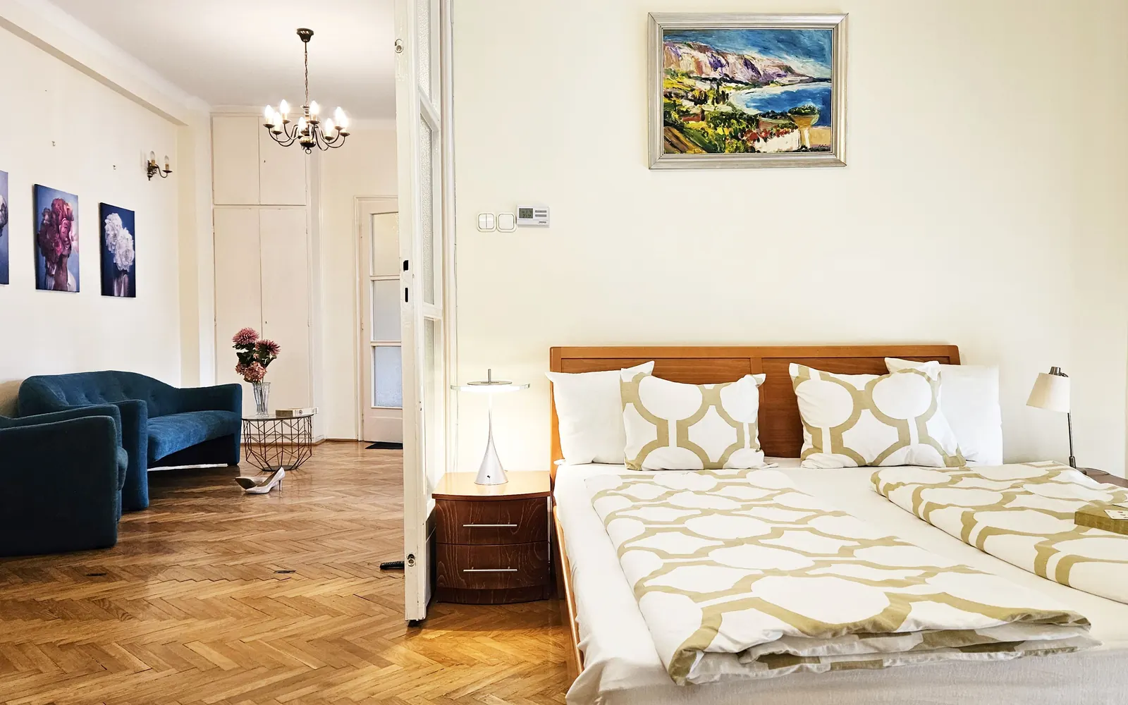 Bedroom with a double bed, the living room with its blue sofa beyond