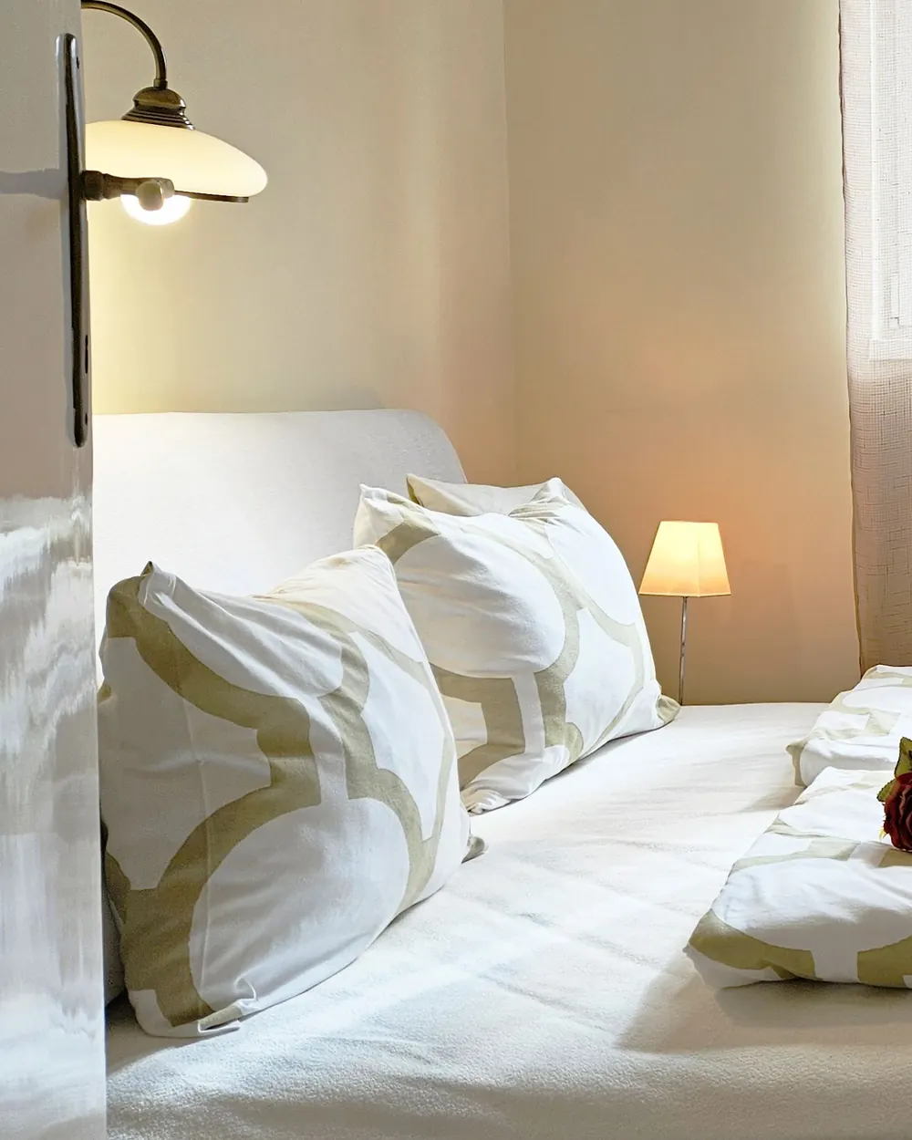 A made bed with a wall lamp and bedside lamp